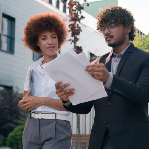 Indian Arabian male man businessman holding papers documents corporate discuss result plans with African American woman colleague businesswoman walking downtown in city multiracial business people. High quality 4k footage